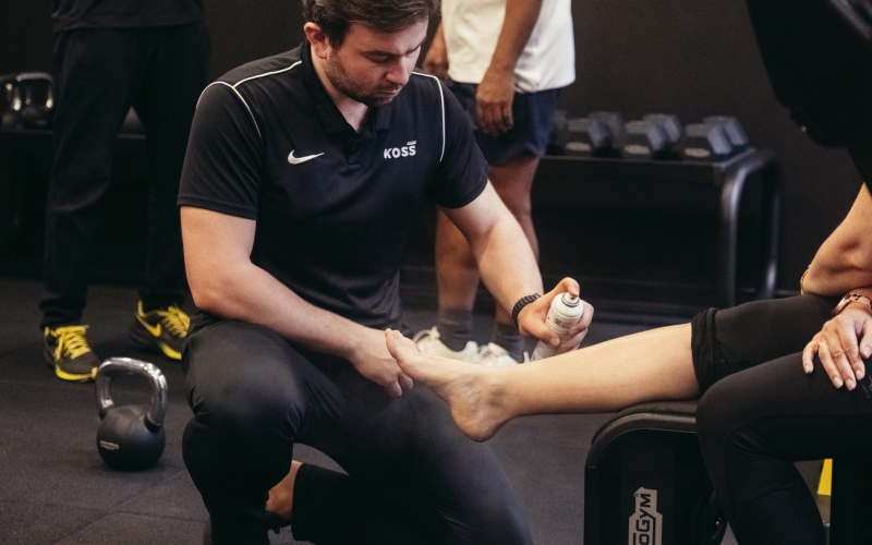 Kinésithérapeute appliquant un spray de récupération sur la jambe d’un patient - Role de kiné | Koss Sport Paris